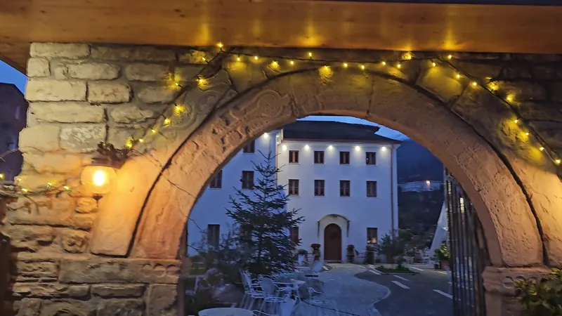 A carved stone arch strung with fairy lights, framing the white wing of the hotel