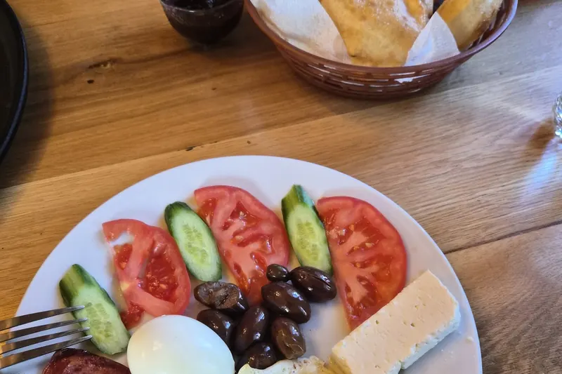 Breakfast plate with fried and boiled eggs, tomatoes, cucumber, olives and white cheese, with a basket of petulla behind