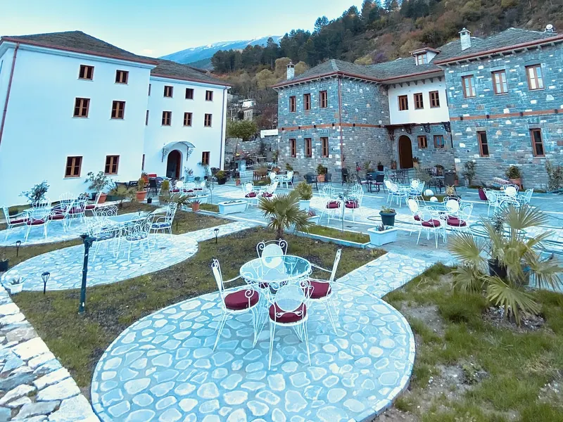 The big courtyard by day: round stone patios, white iron chairs with red cushions, palms and both wings of the hotel