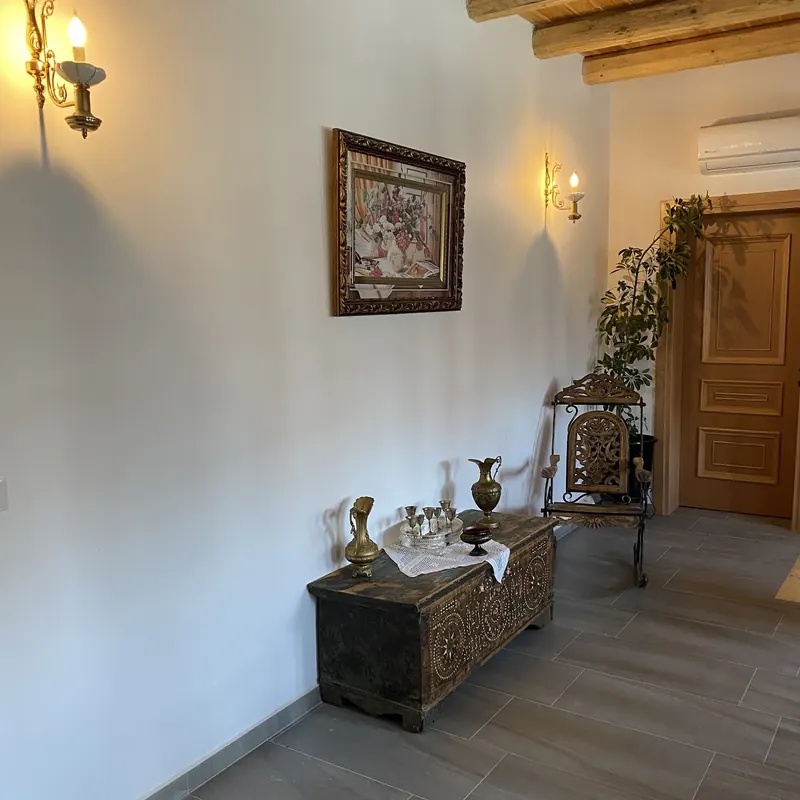 A hallway with a timber ceiling, wall lamps, a framed painting and a carved wooden chest