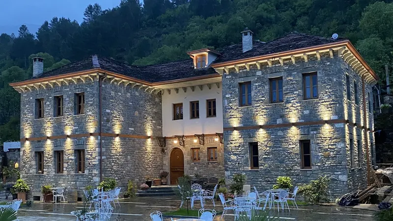 The two stone wings of the hotel lit at dusk, with white iron tables on the wet courtyard