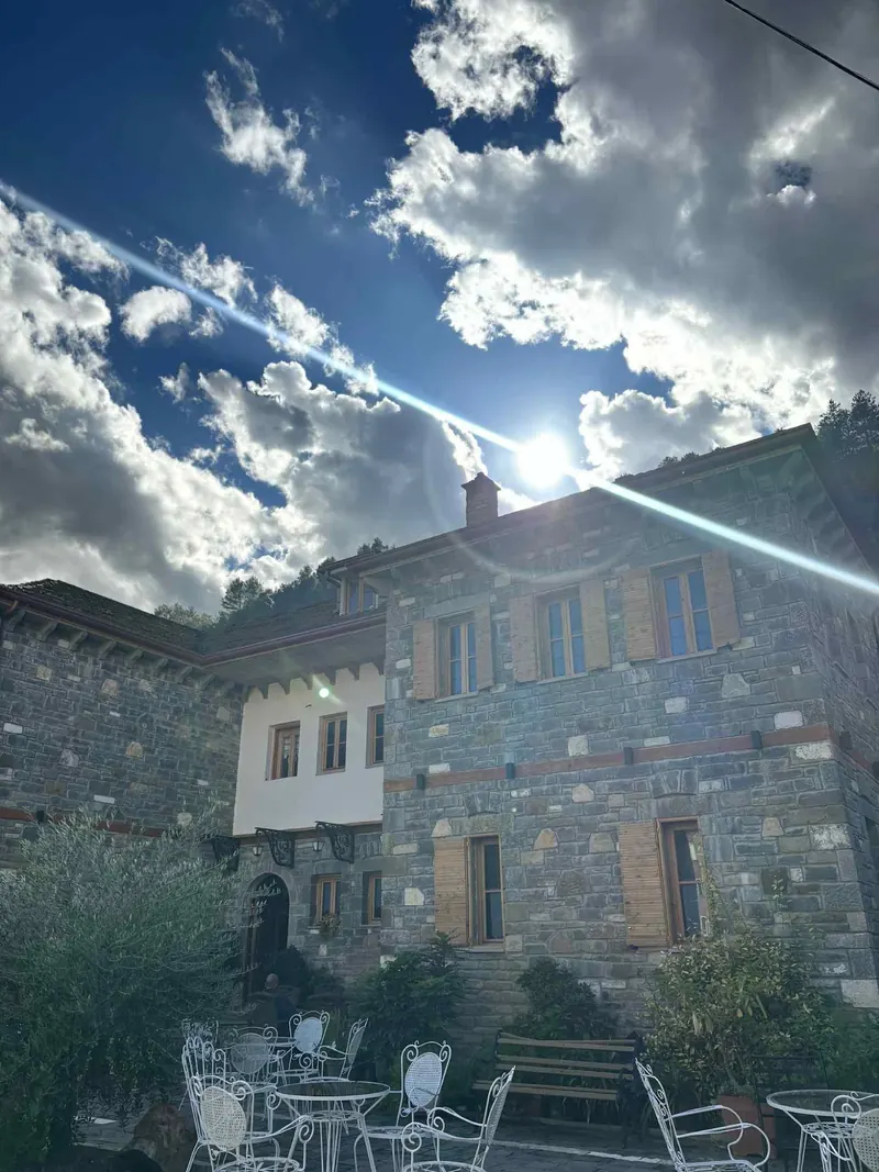 The hotel's stone wing and white upper floor under a bright sky with the sun breaking through clouds