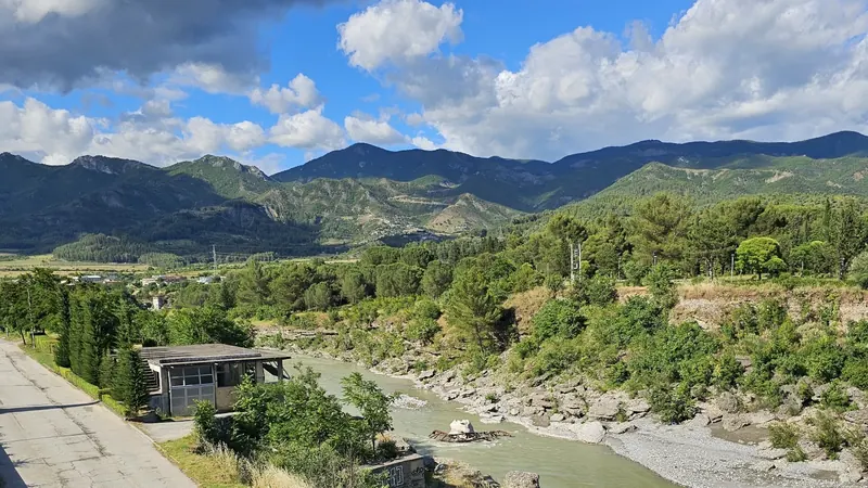 The Vjosa river valley near Përmet, green banks and mountains under a big sky